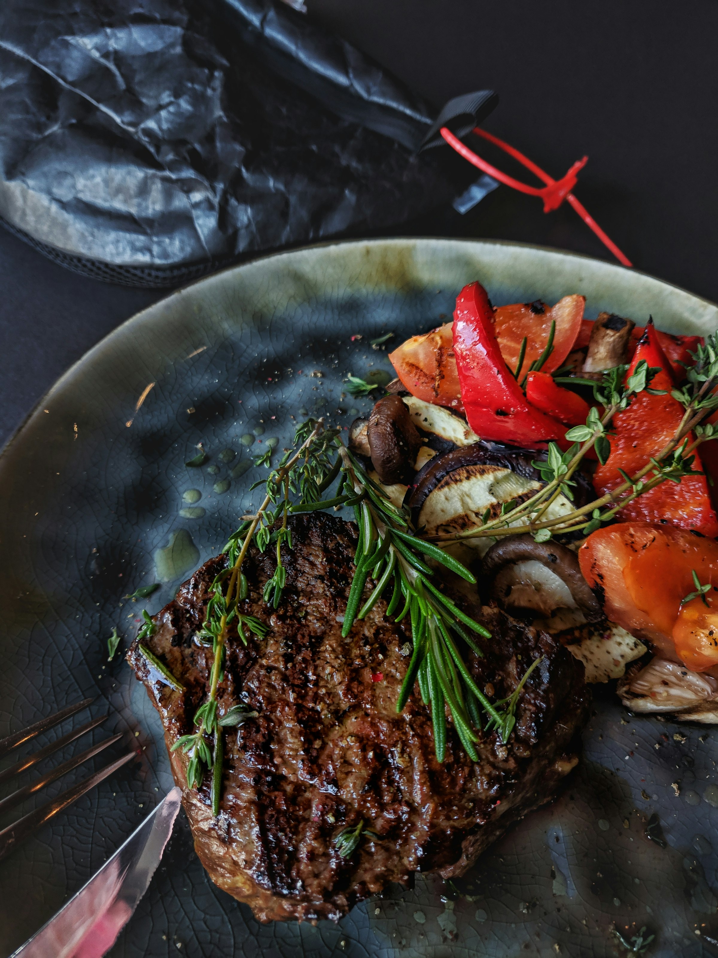 Grilled fillet steak with charred rosemary, thyme and heirloom tomatoes on a dark plate