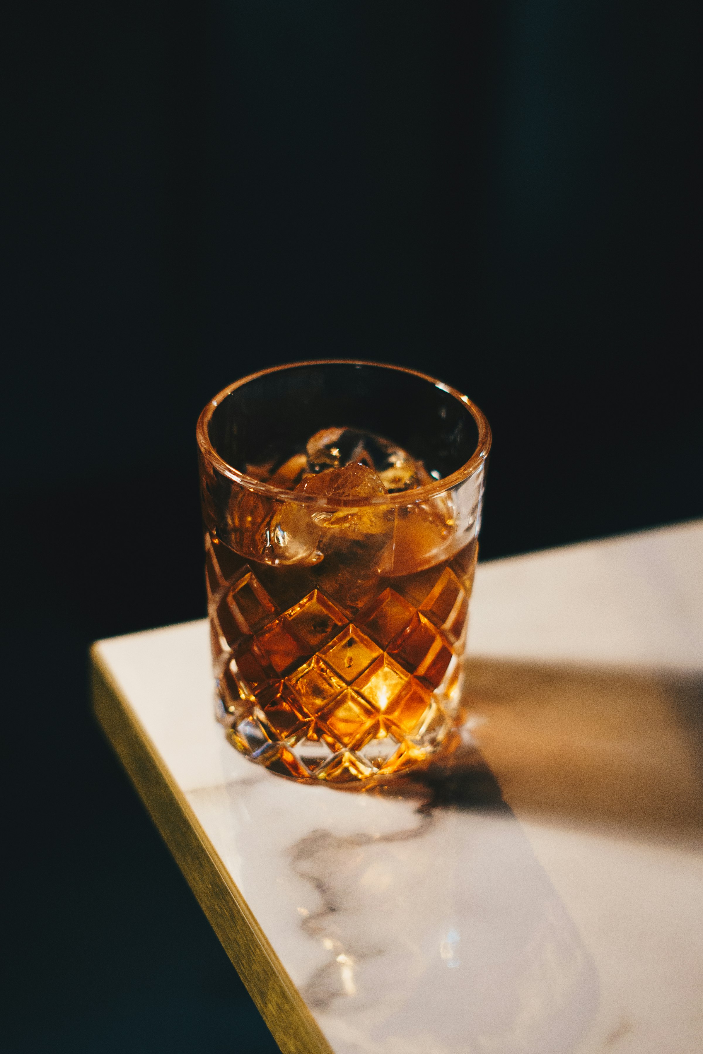 An old fashioned cocktail with ice on a dark marble bar top
