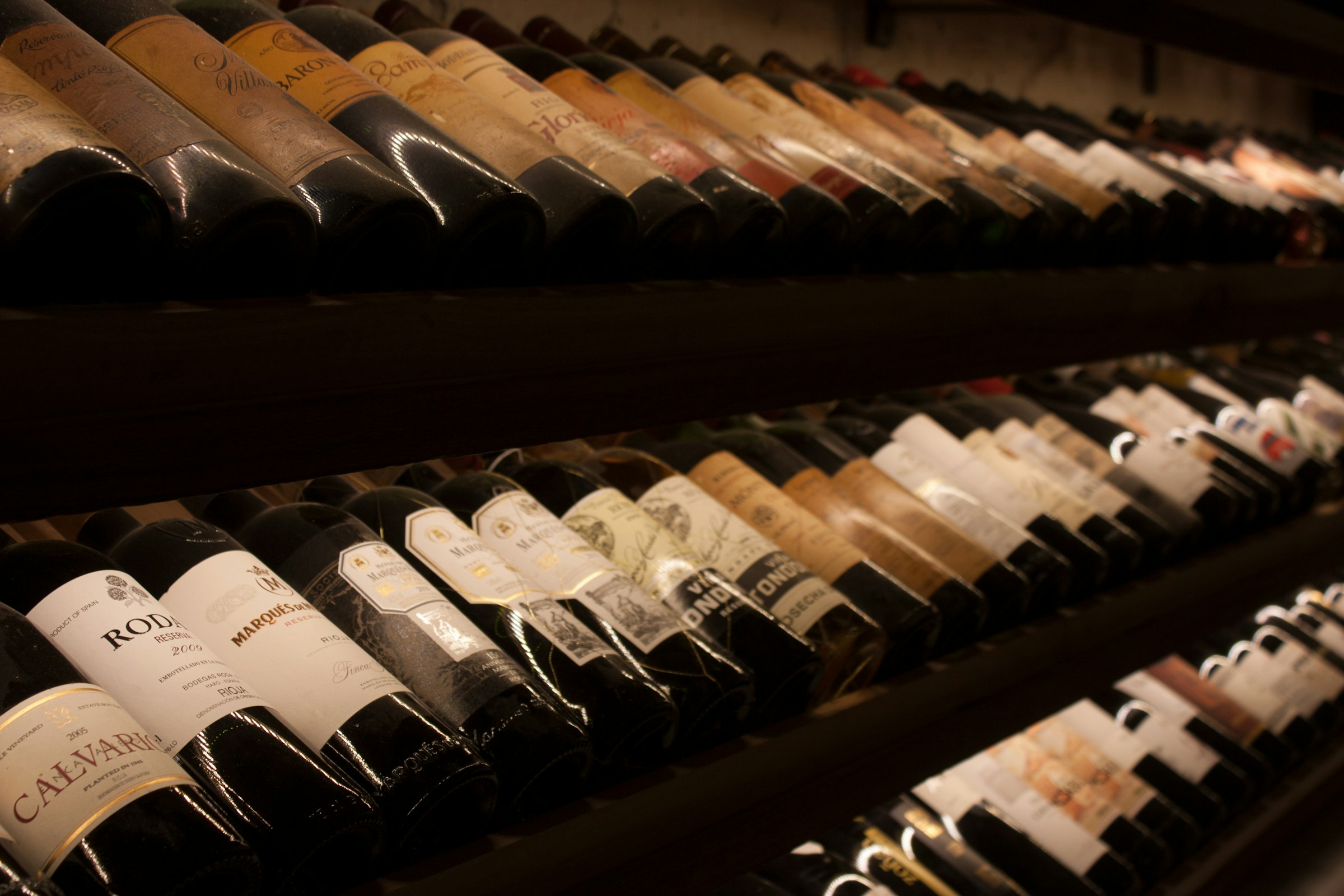 Rows of aged red wine bottles on dark wooden racking